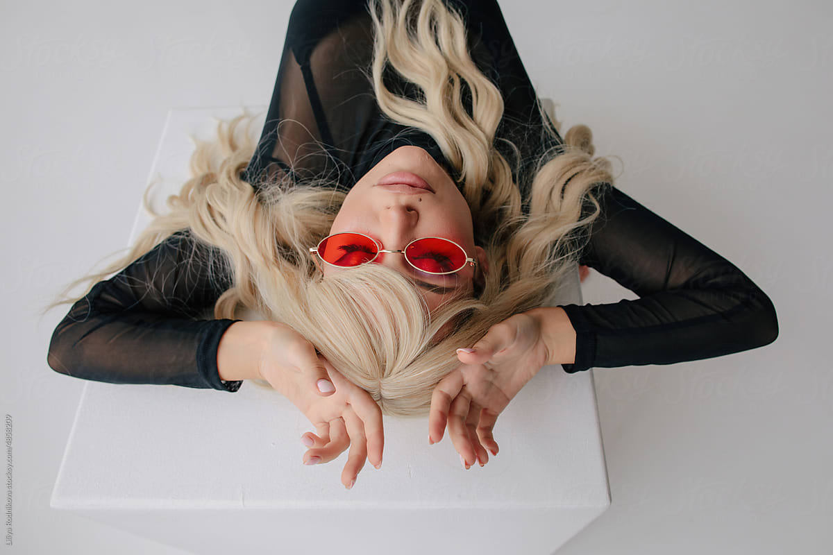 Stylish blond woman lying on cube