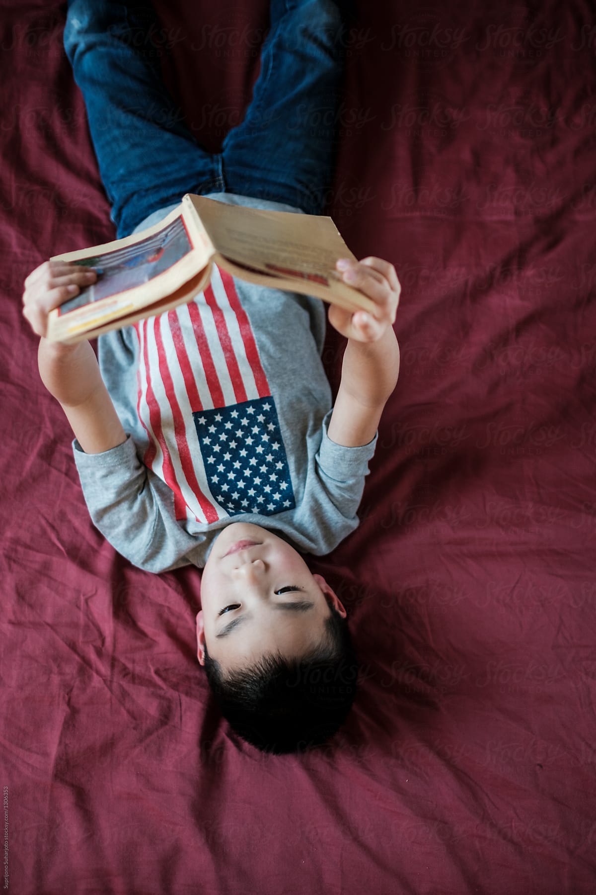 Asian kid reading a book on bed