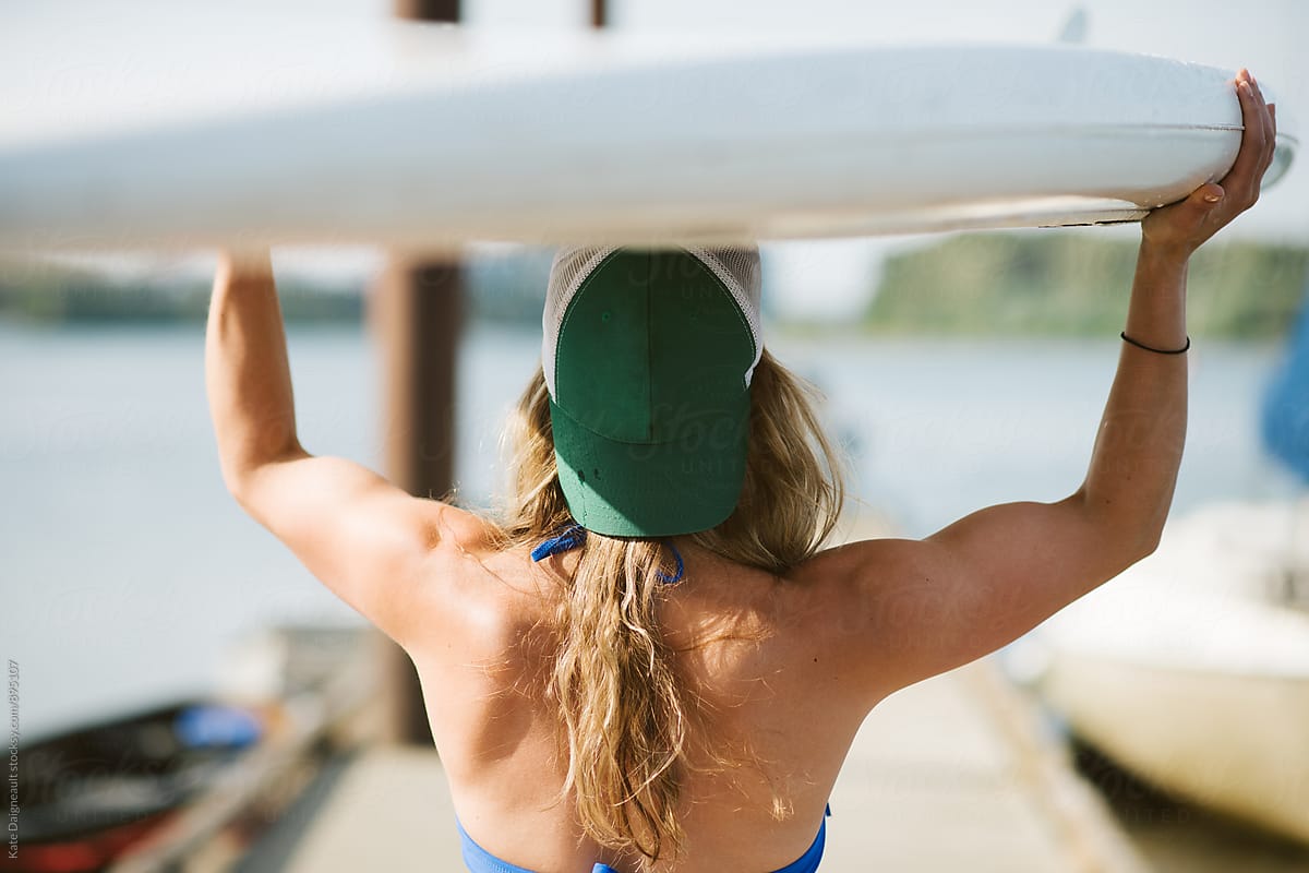 Young blonde fit woman on a dock with paddle board.