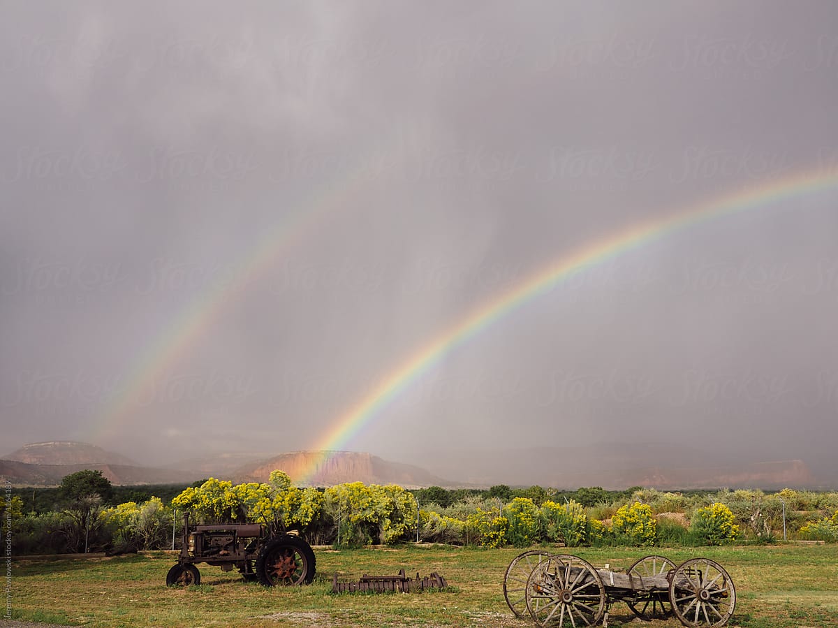 Double rainbow after storm over rusty tractor and wagon
