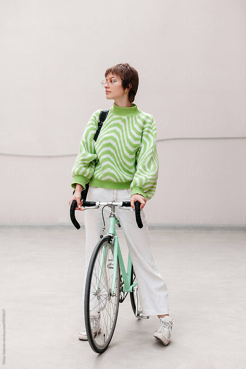 Young woman with bicycle on gray urban wall background