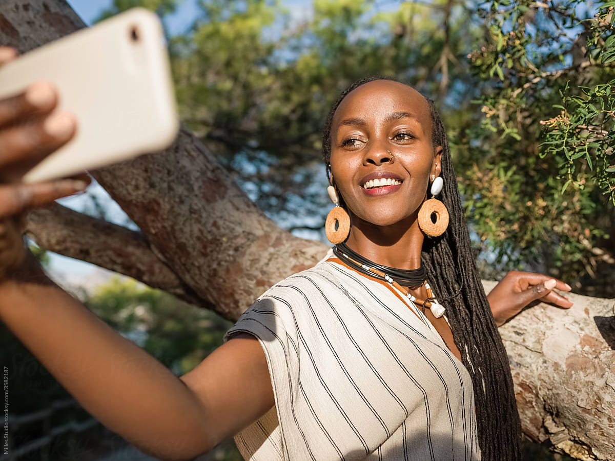 Black woman taking selfie near tree