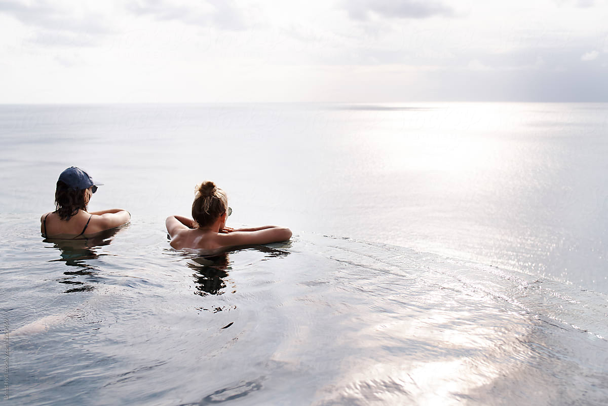 Two Young Attractive Women Relaxing In An Infinity Pool By Brent Hyll 