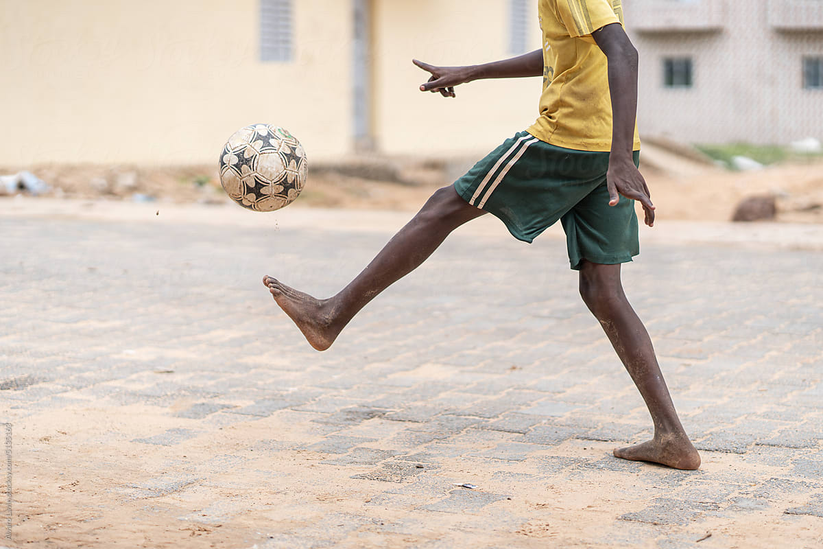 Crop child kicking ball on street