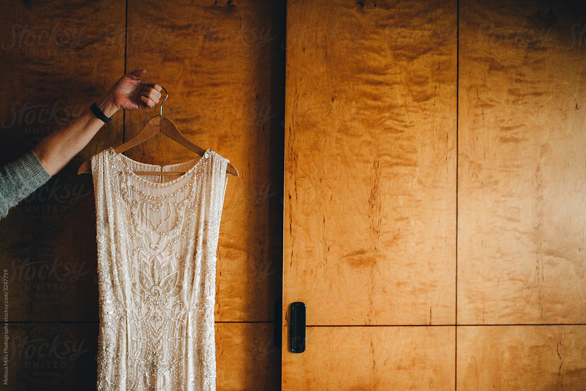 anonymous hand holding a bridal dress on a coat rack in front of a wooden closet
