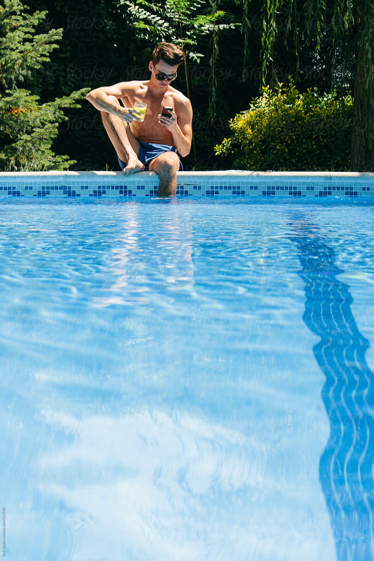 Young Man Sitting And Using His Phone In A Pool by Stocksy Contributor Inuk  Studio - Stocksy