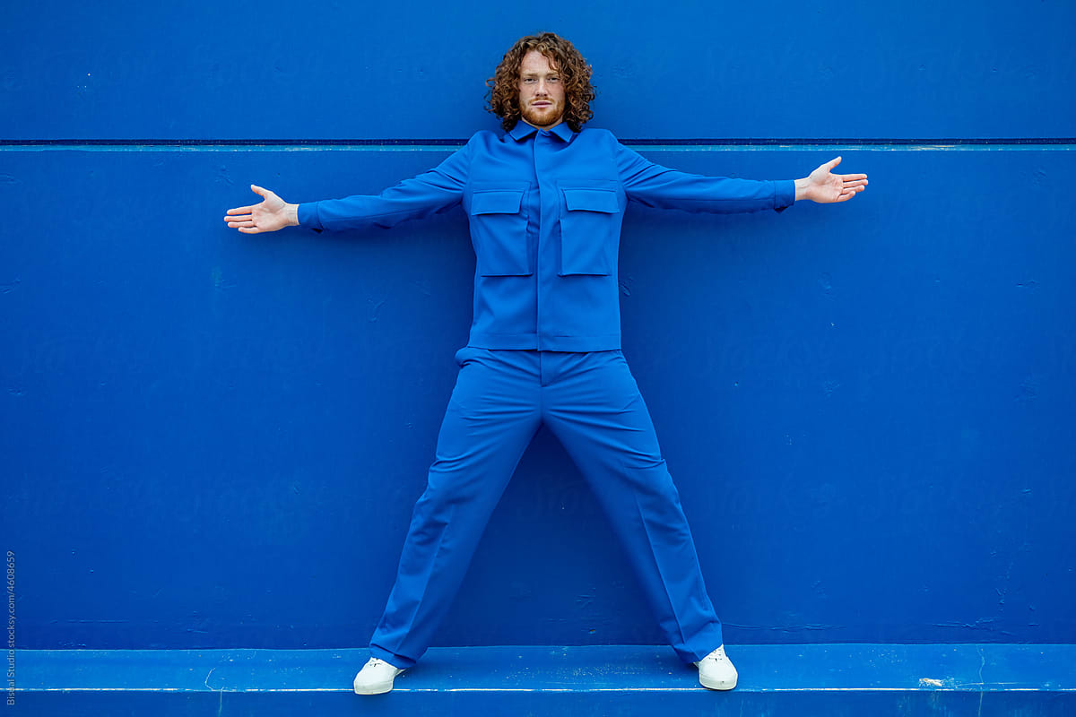 Man spreading arms and legs against blue wall