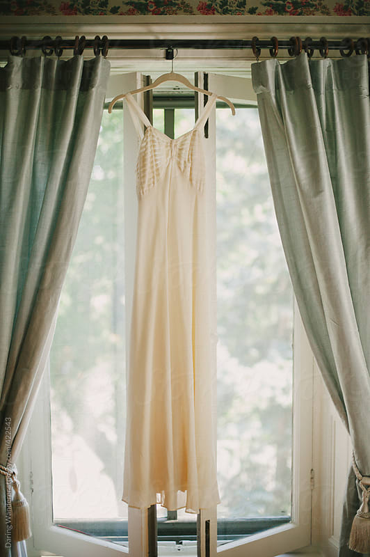 Vintage wedding dress hanging in window by Daring Wanderer - Stocksy United