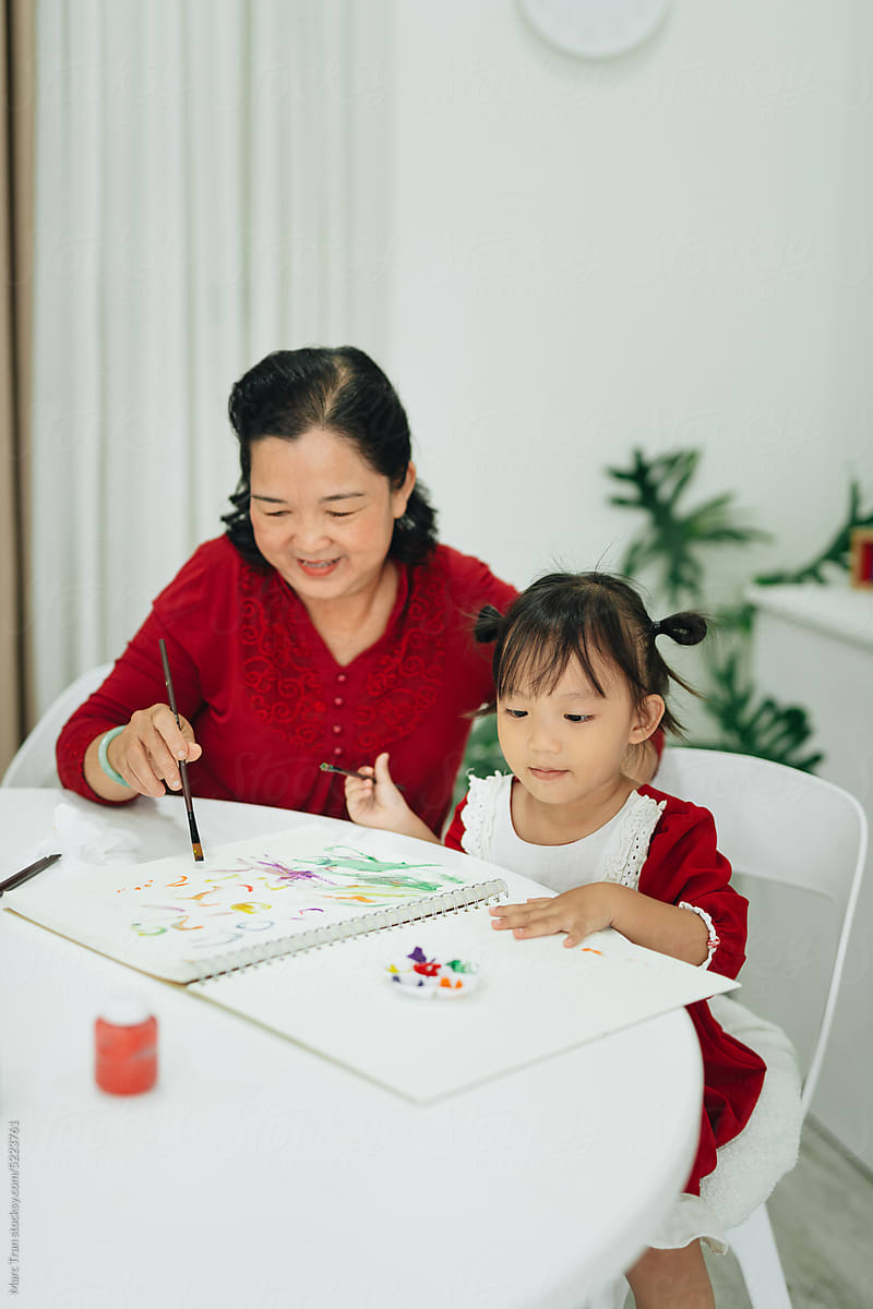 Happy grandmother and little daughter drawing at home,
