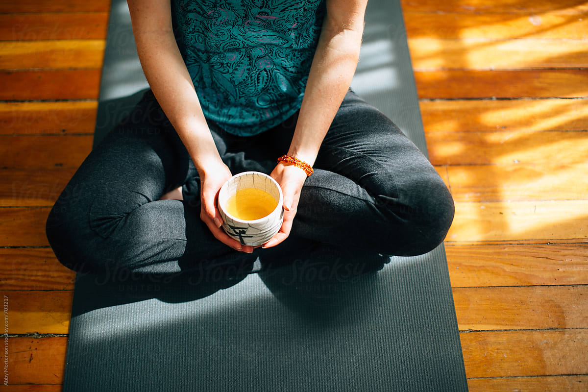 Woman sitting on yoga mat with teacup