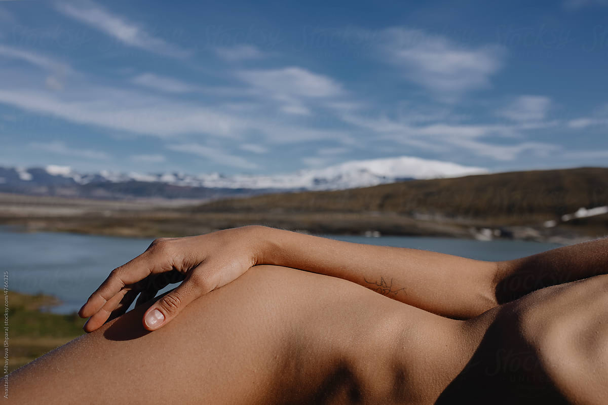 Naked woman lying in front of the river and snowy mountains in Iceland