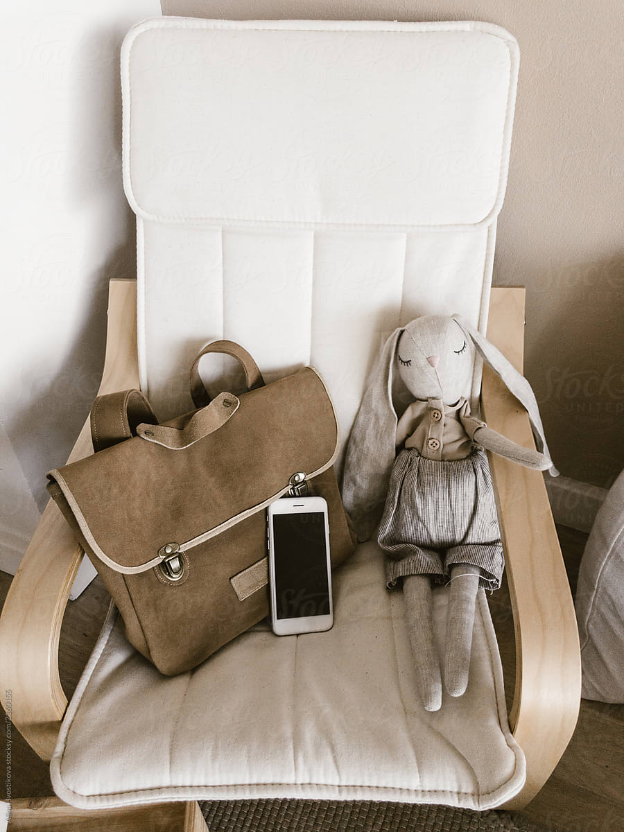 Smartphone near bag and toy on armchair