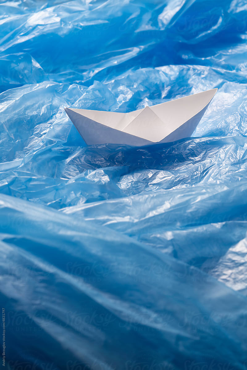 Paper ship swim through the ocean from plastic bags