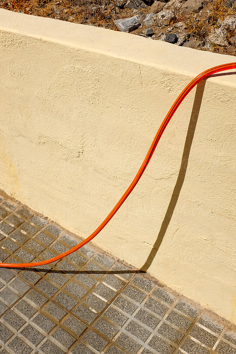 An orange hose and its shadow on a wall.