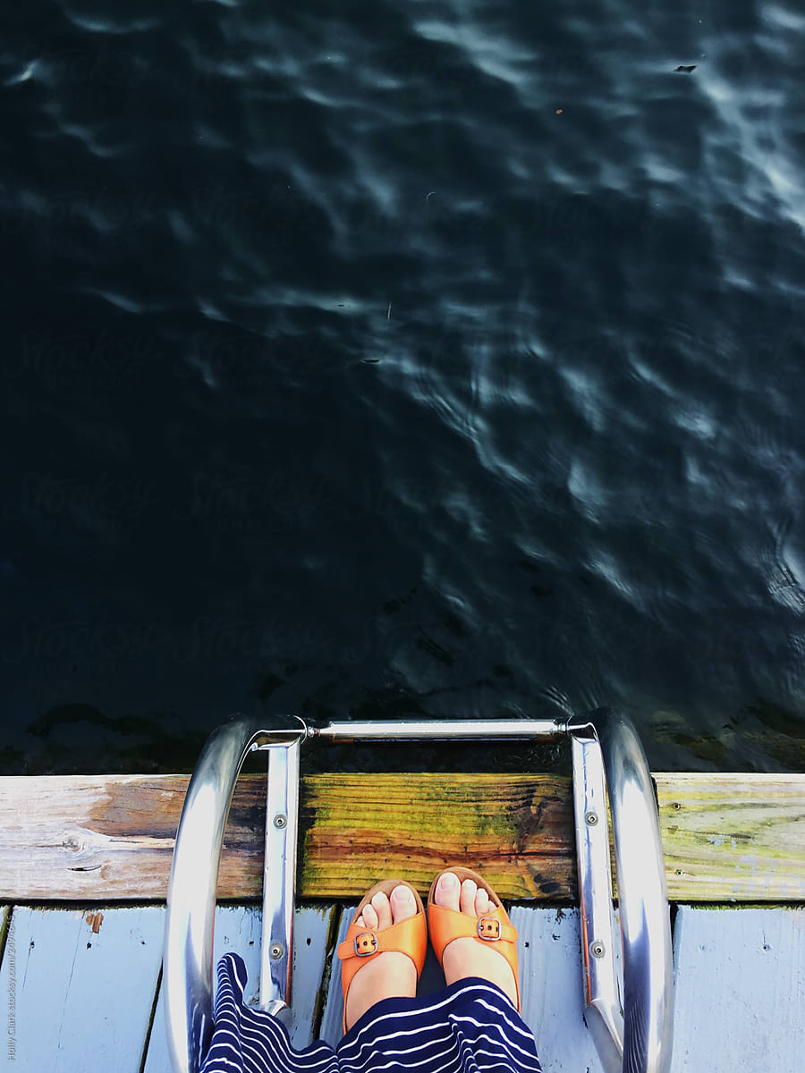 Woman\'s feet on dock next to lake between swim ladder