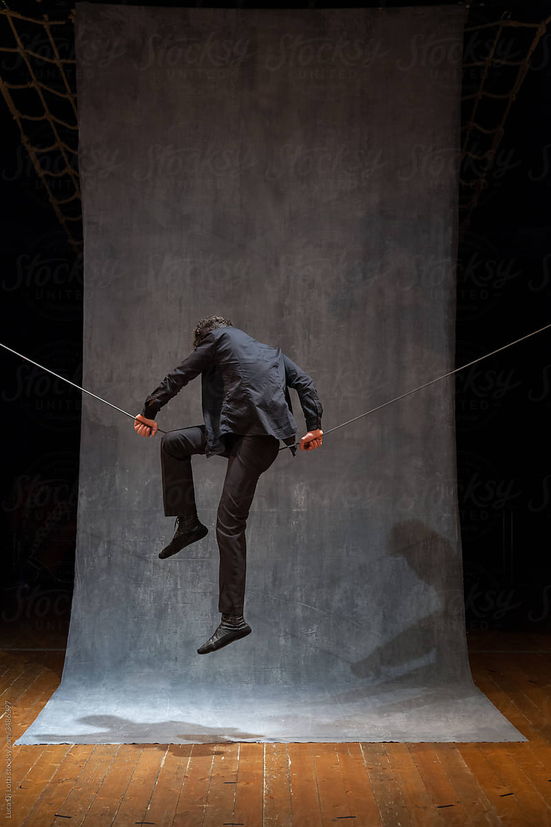 Circus performer climbs on a slackwire wearing black clothes.