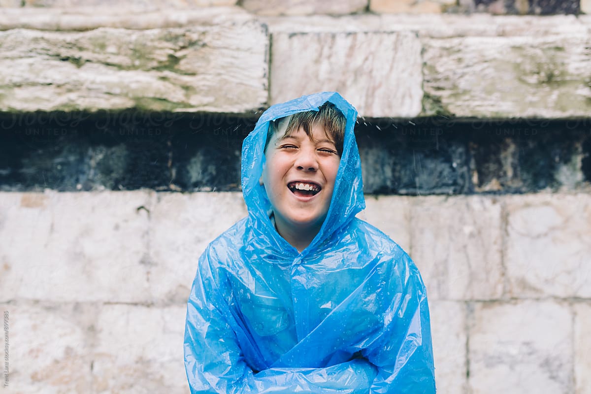 Cheerful boy wearing wet raincoat laughing in the rain