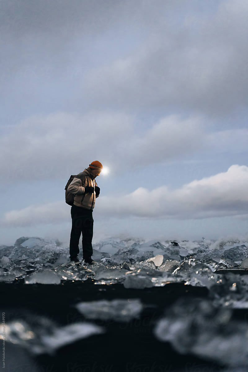 Traveler stands among ice blocks and glaciers, illuminated by headlamp