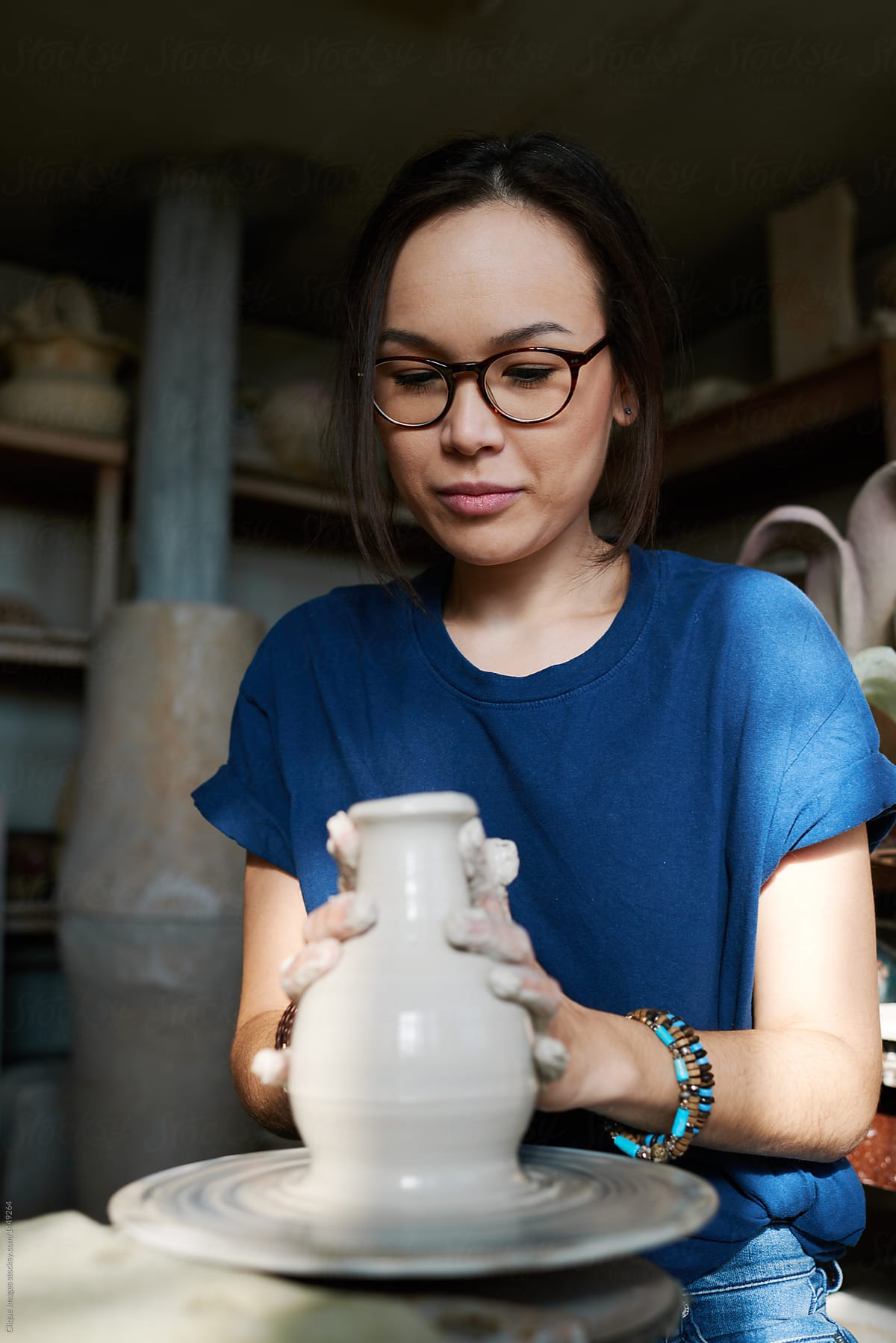 Modern potter woman making clay vase in small ceramics shop by Clique