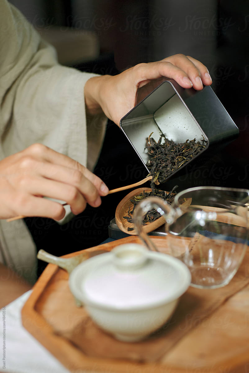 Women's hands put dry Chinese tea leaves into a wooden chahe