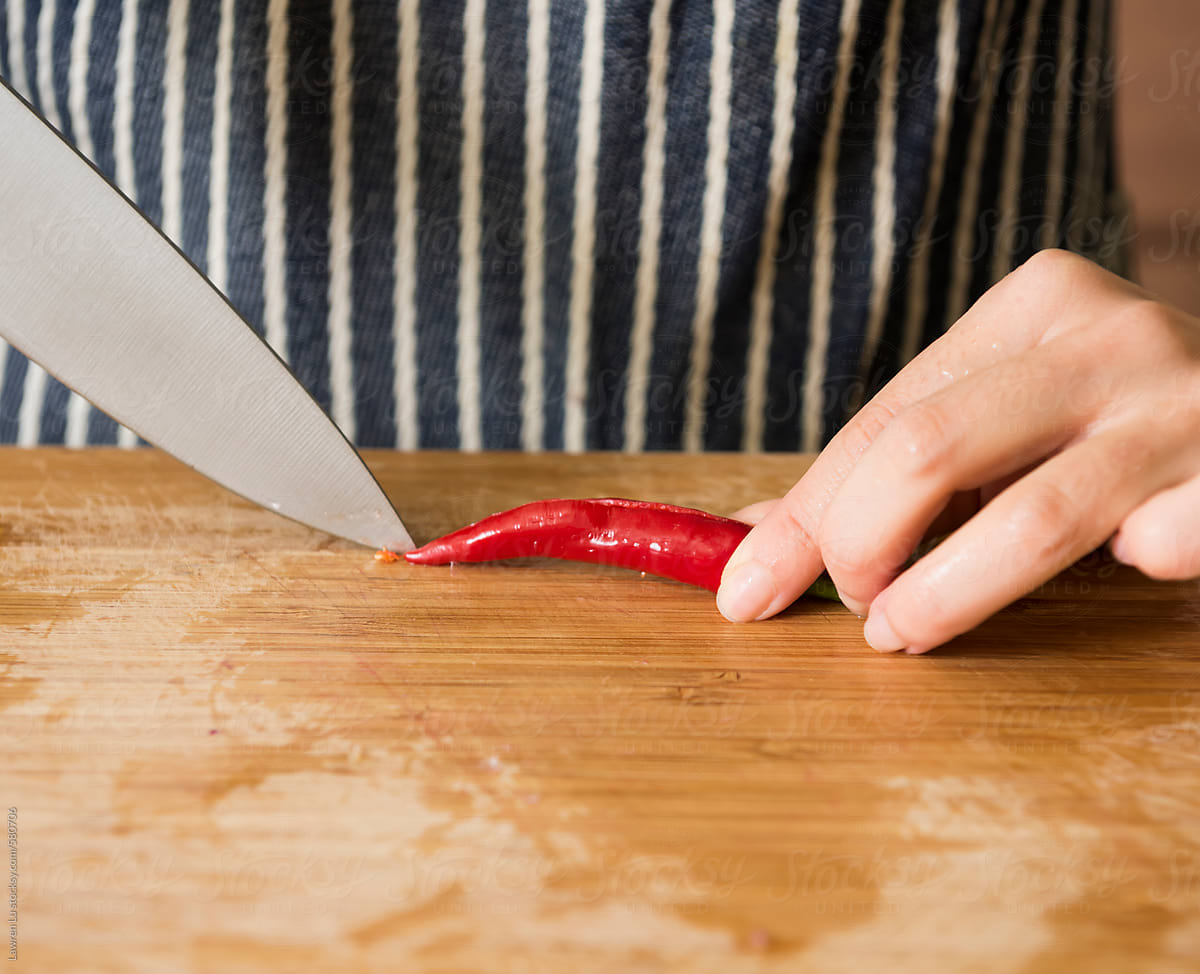 Female hands cutting red chili in kitchen background.