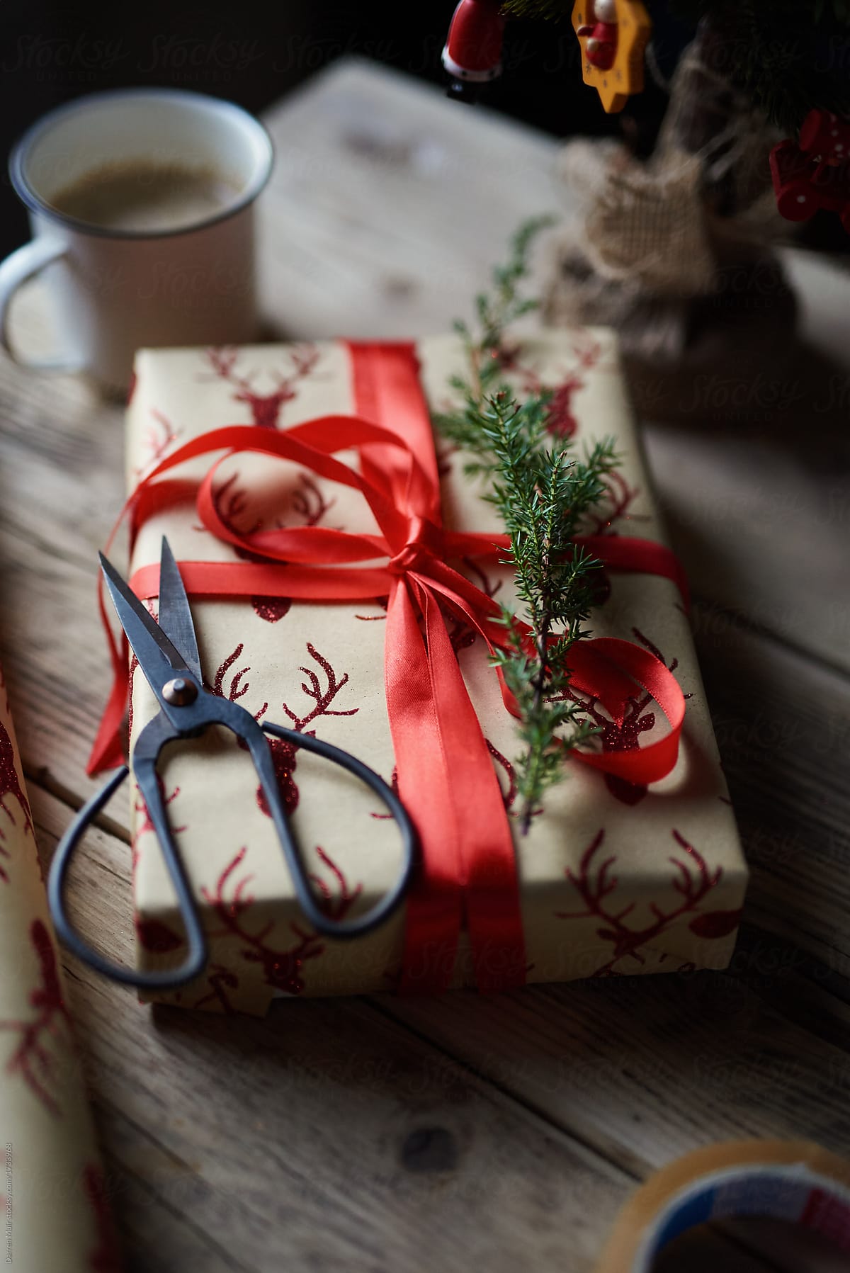 Christmas gift wrapped present in reindeer print brown paper with red bow on wooden table.