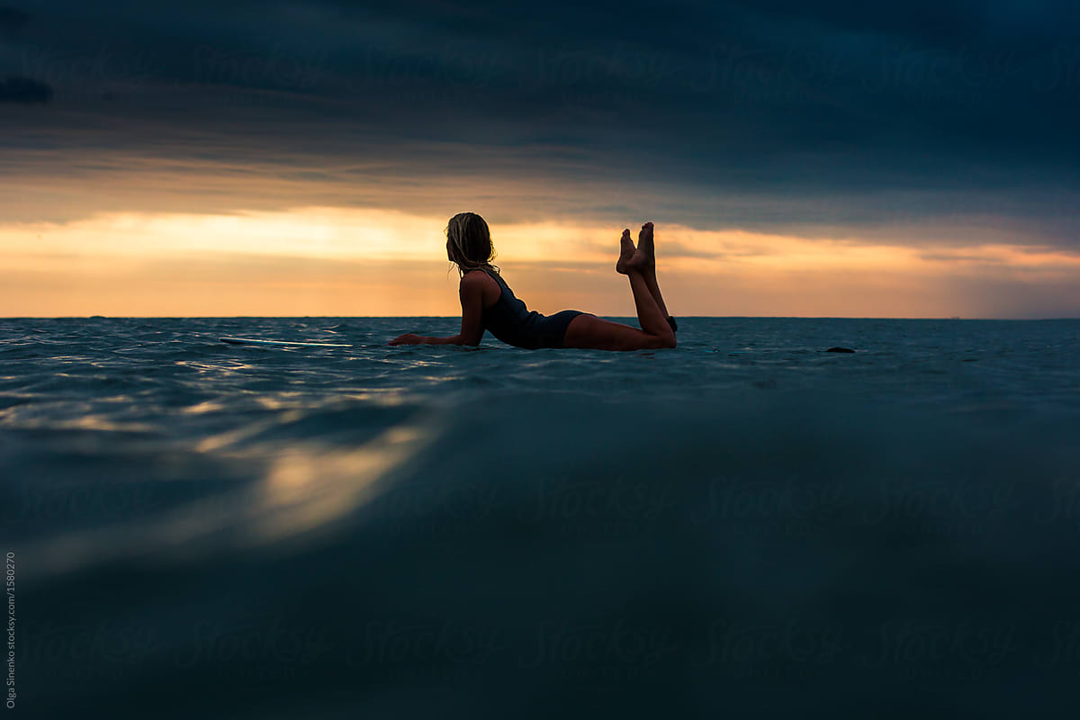 Silhouette of woman in the ocean lying on surfboard at sunset. Beautiful clouds. Vivid colors.