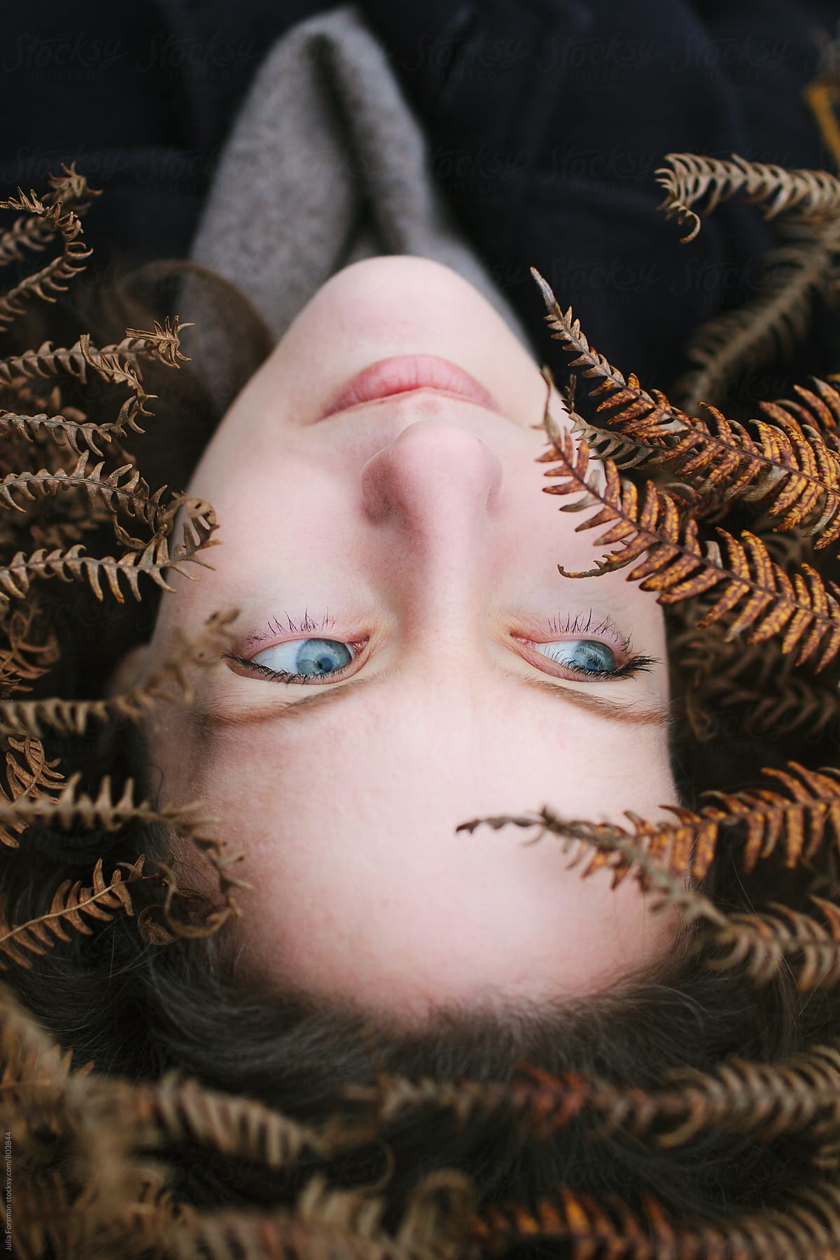 Beautiful blue eyed woman lying among autumn ferns