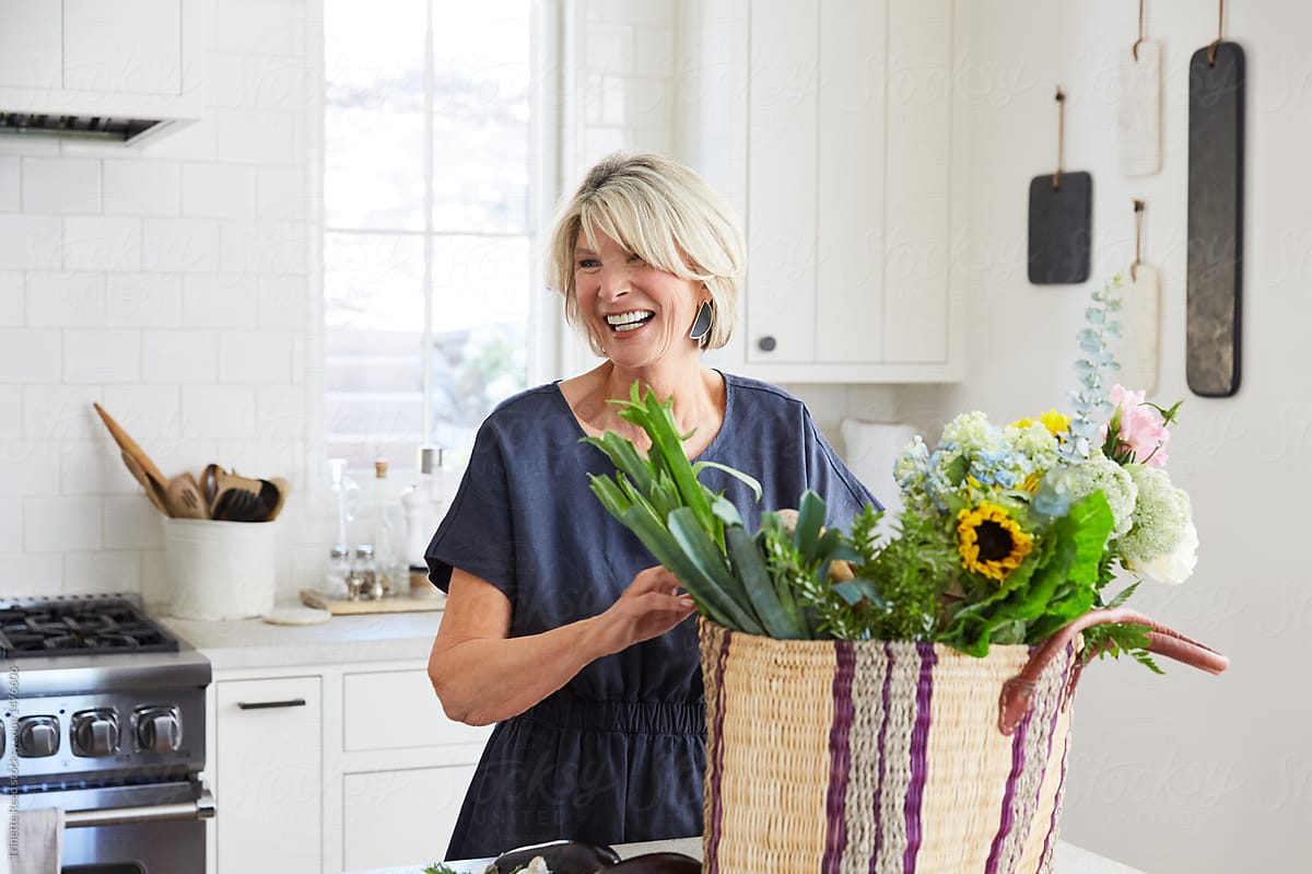 Senior woman in kitchen with farmers market basket with vegetables and flowers
