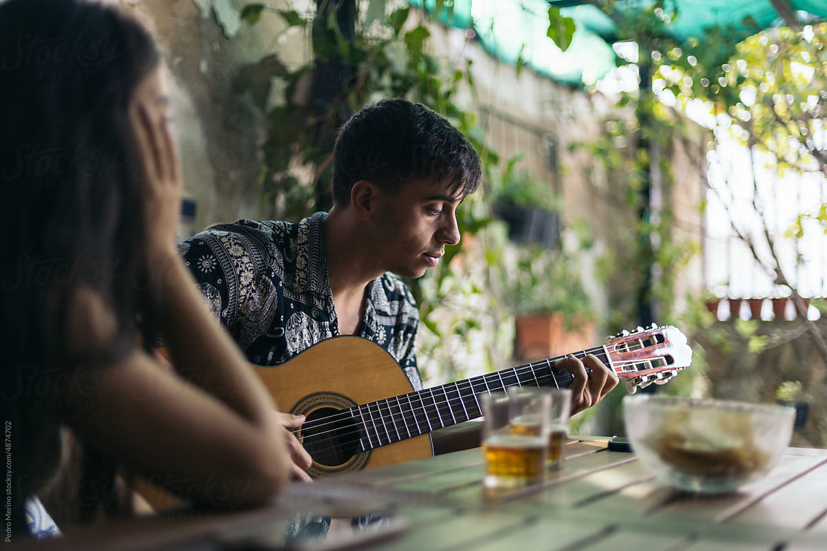 Young man playing the Spanish guitar in a patio with his friend