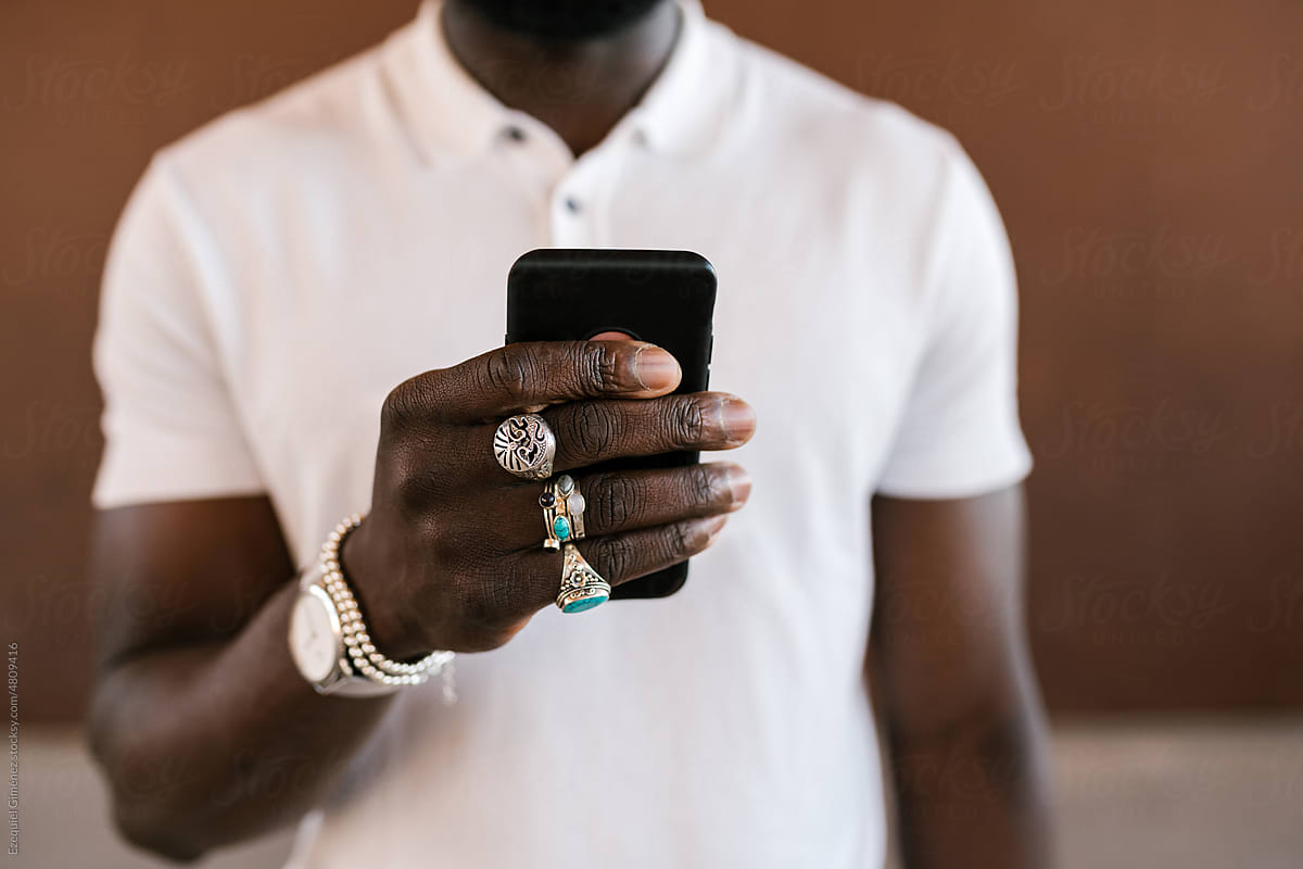 Crop black guy in stylish accessories using smartphone