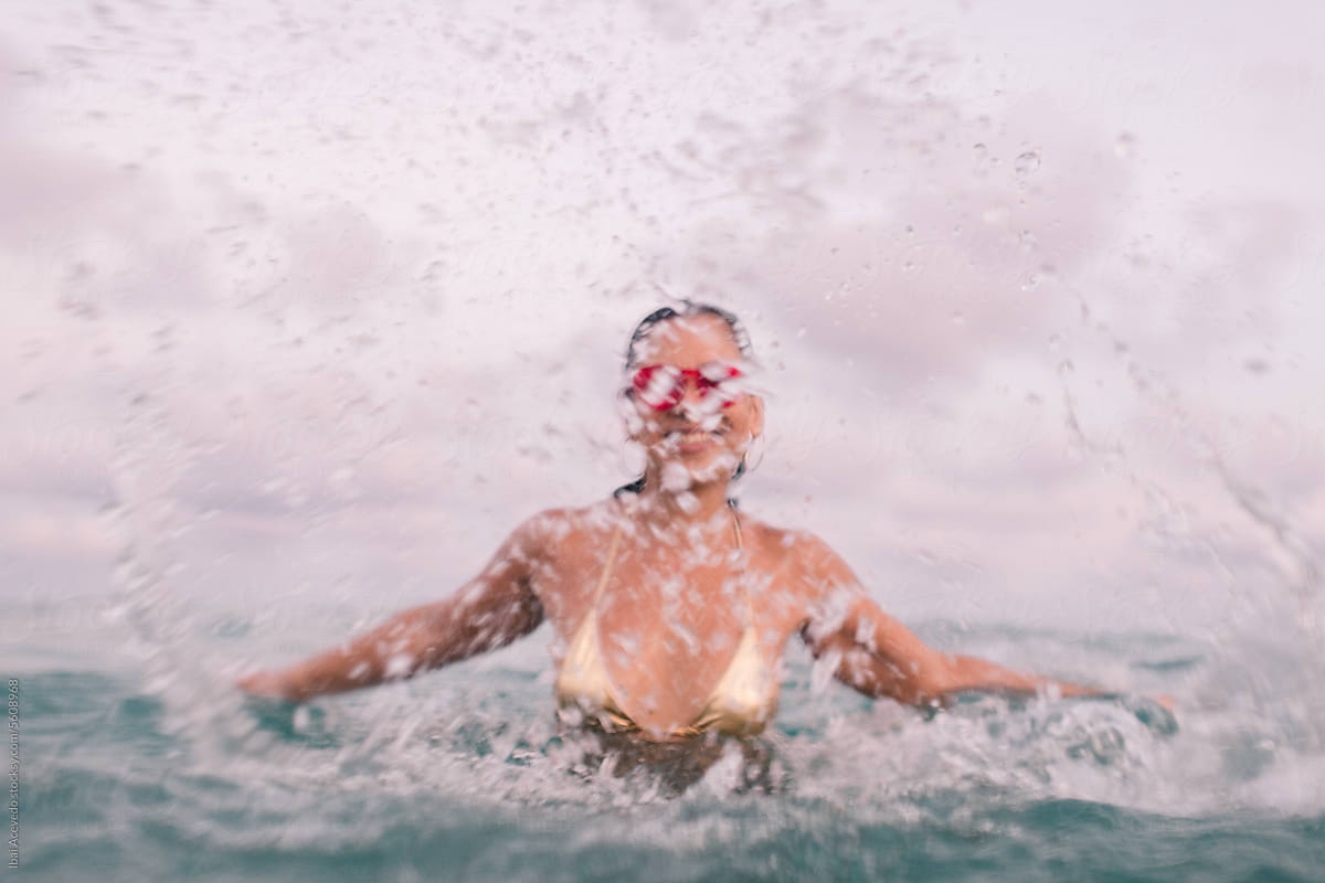 Cheerful woman splashing sea water towards camera