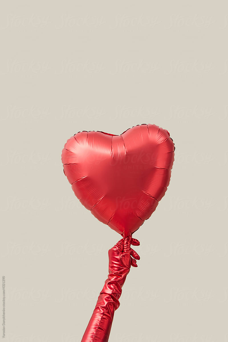 Woman's hand in glove holding red heart shape balloon