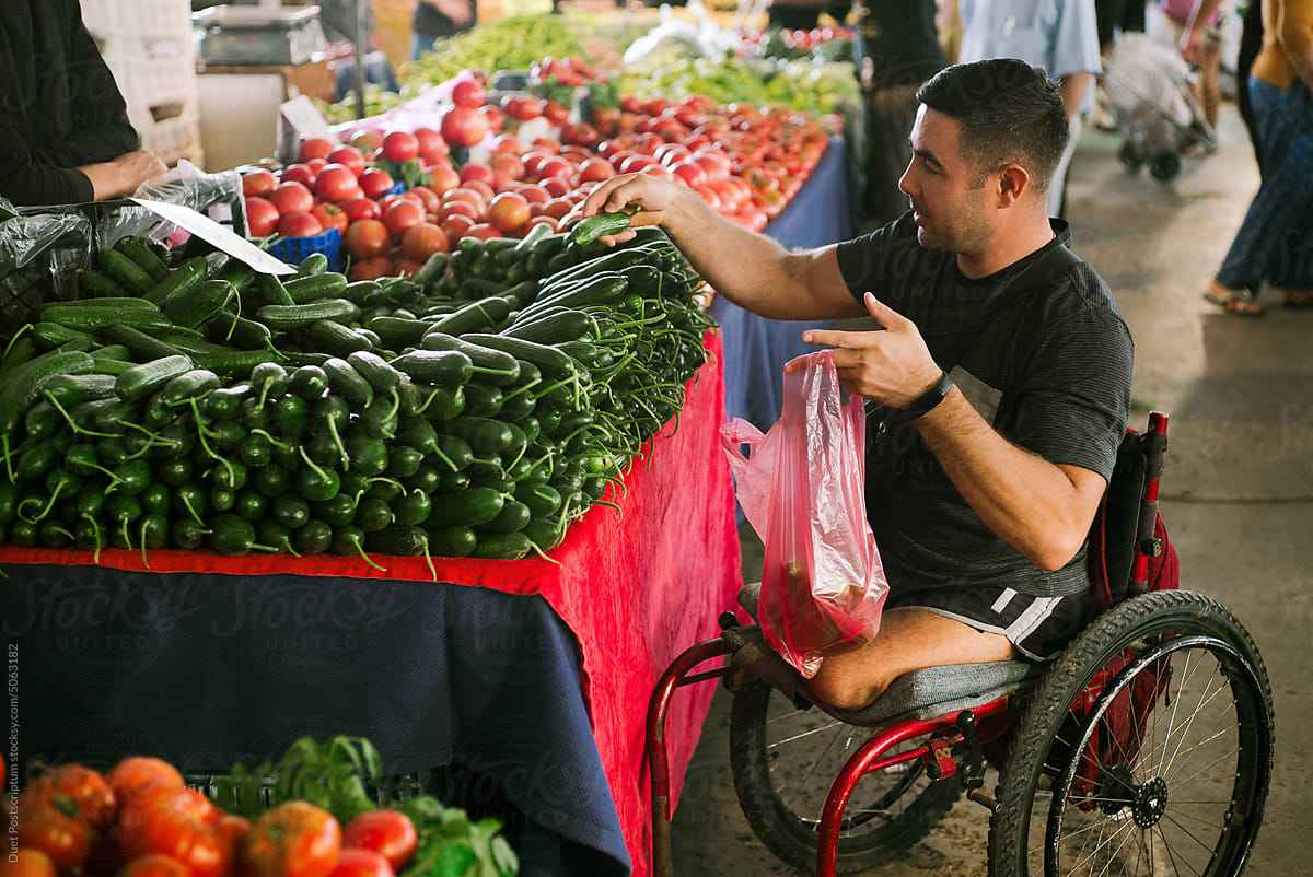 Adult man on a wheelchair chooses fresh cucumbers at a street market