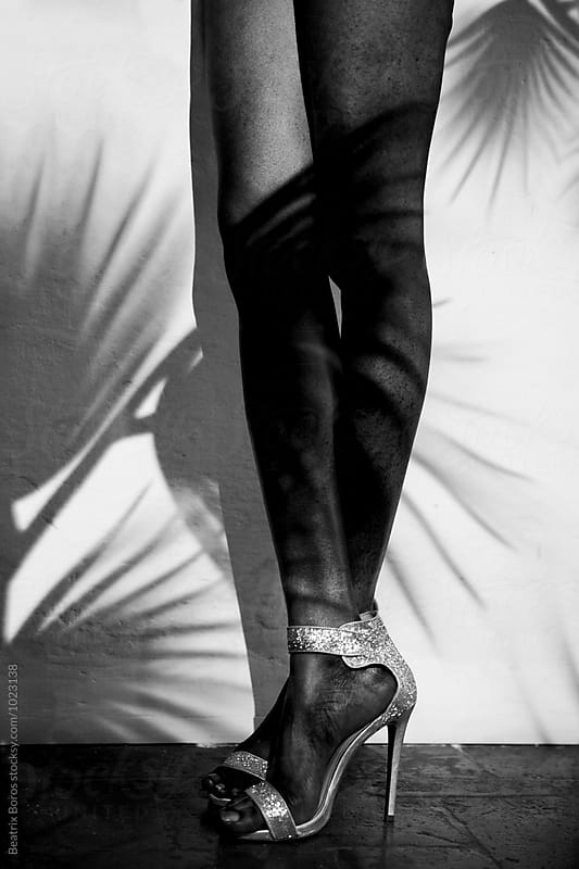 Black woman\'s long legs in sandals with palm leaf shadows