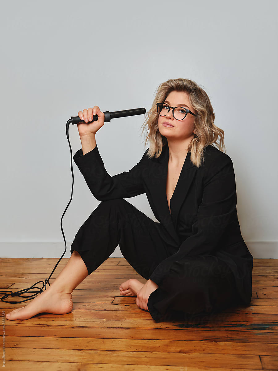 Hairdresser with curling iron sitting on floor in studio