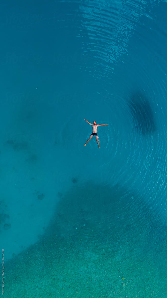 young athletic man relaxing in turquoise water, drone overhead