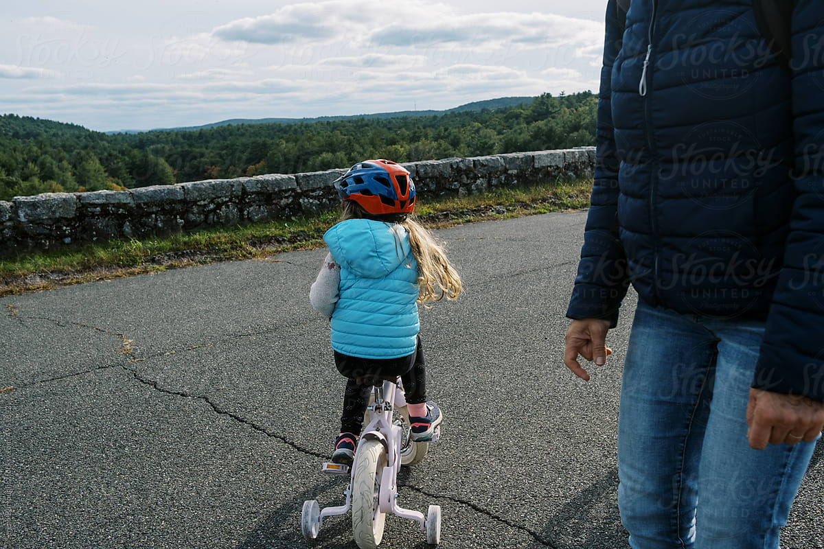Little girl riding her bicycle with training wheels and a helmet