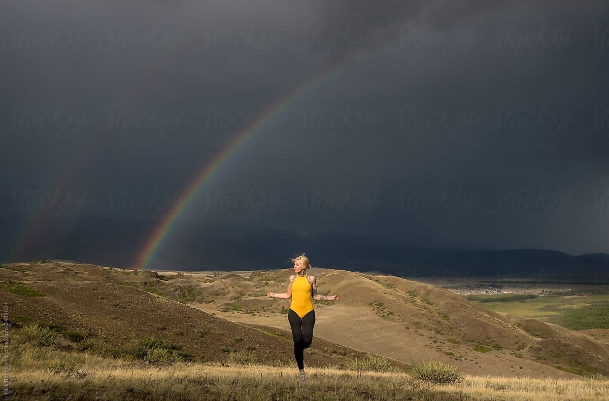 Young woman jumping with Jump rope in the natural area with mountains and rainbow on the background