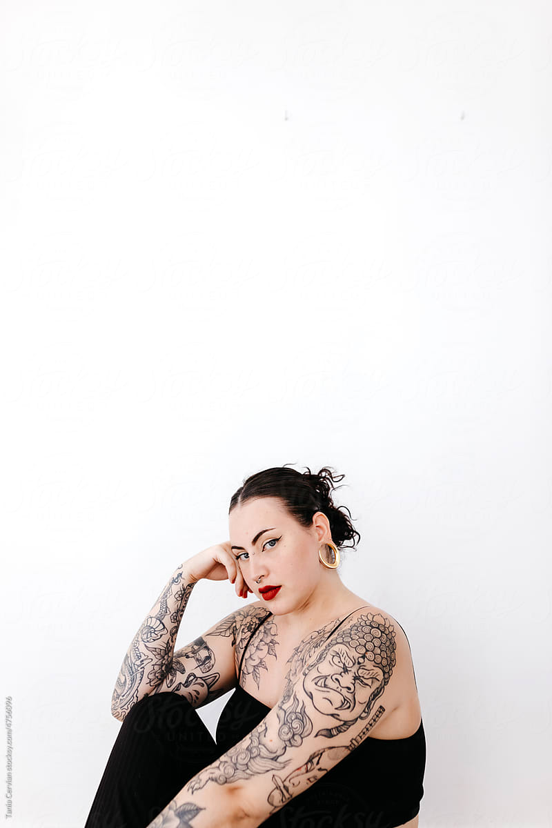 Trendy tattooed woman sitting near wall