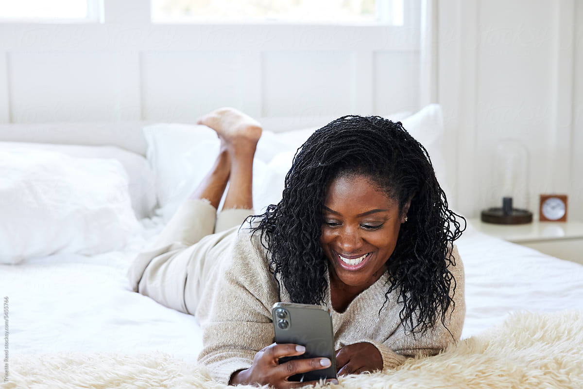 Mature Black woman watching her phone at luxury home in bed smil