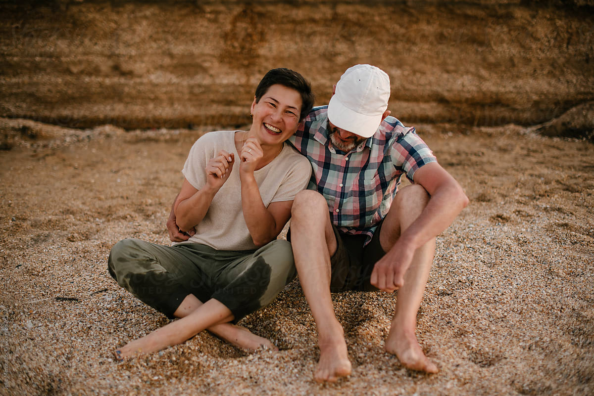 An adult couple are sitting on the beach and laughs together