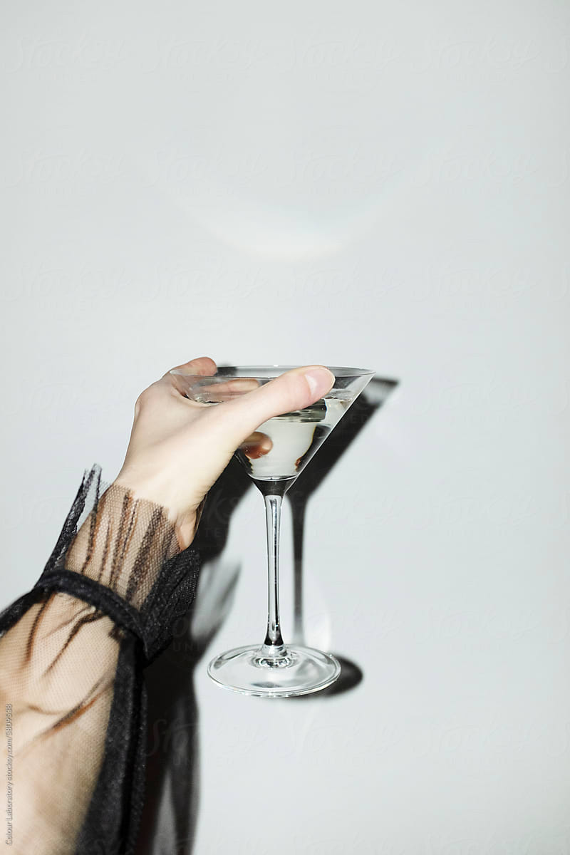 Hand with elegant ruffled mesh shirt holding martini glass with drink