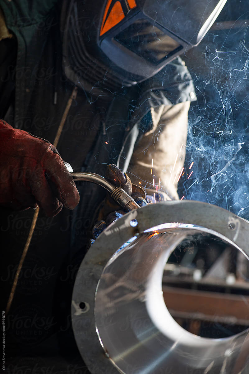 Male welder wearing a protective mask is welding stainless pipe