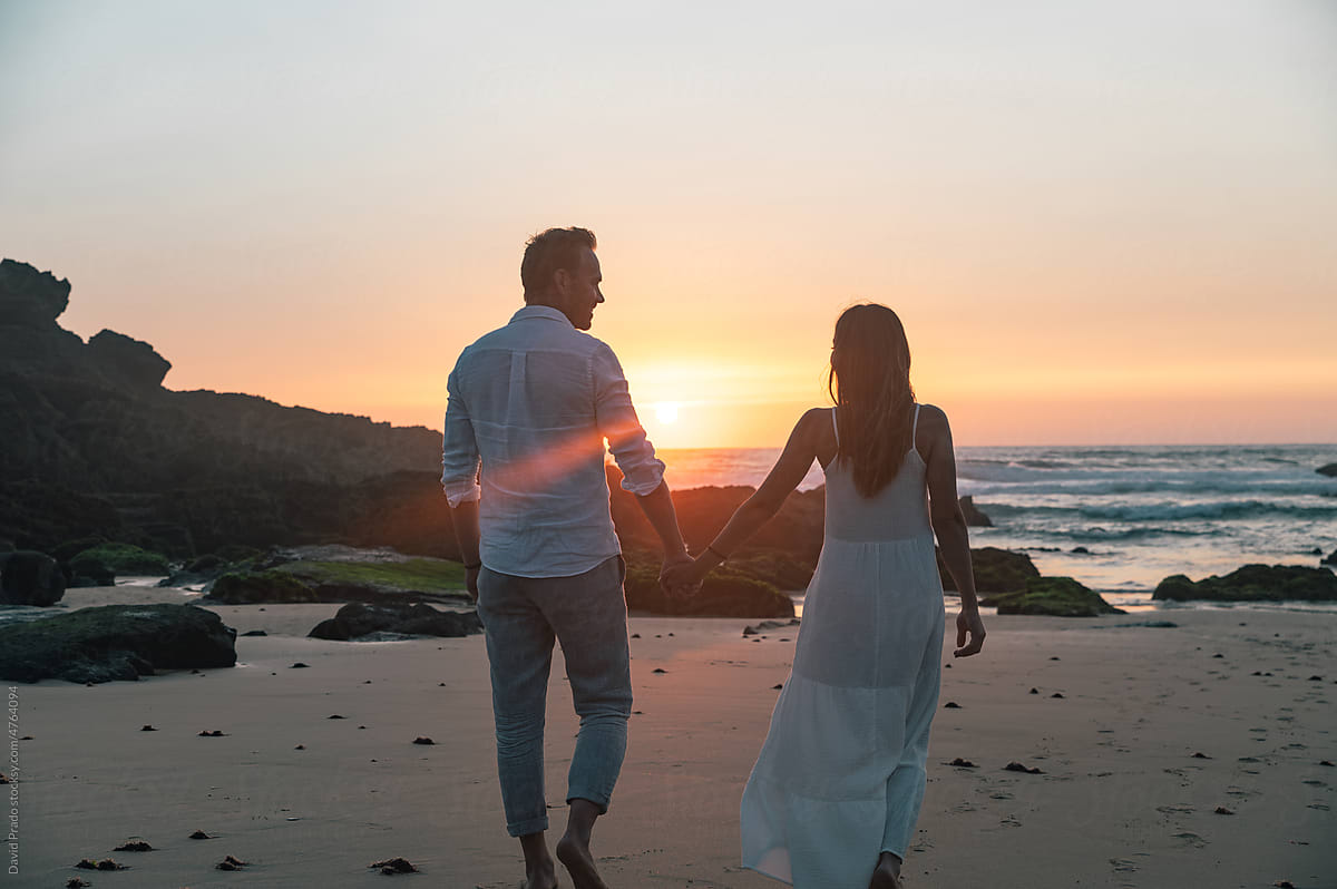 Anonymous couple holding hands on seashore at sunset time