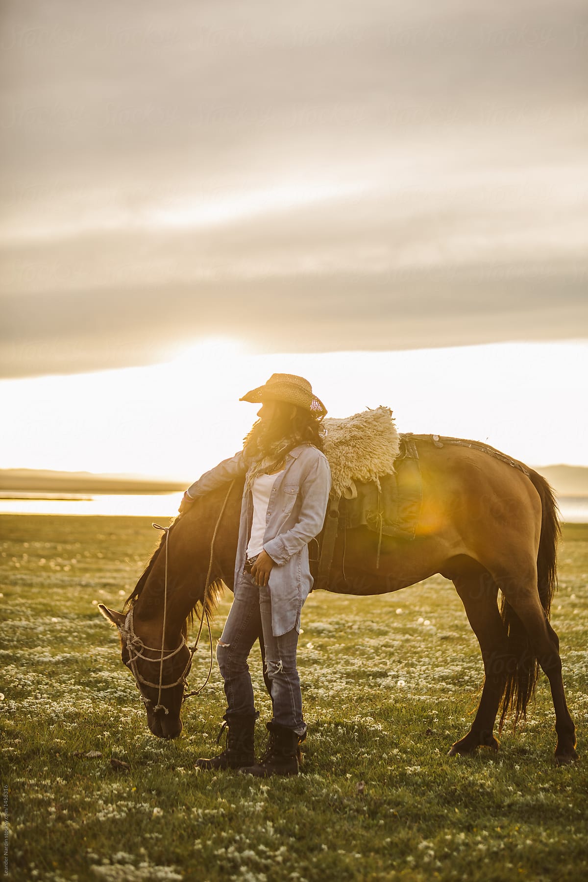 cowgirl standing beside a horse at sunset