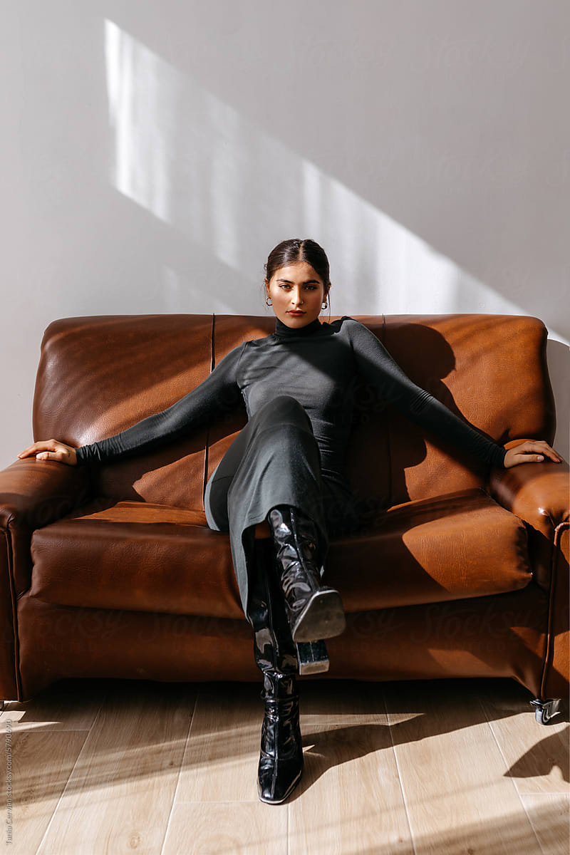 Stylish woman in black body fit cloth sitting on leather couch