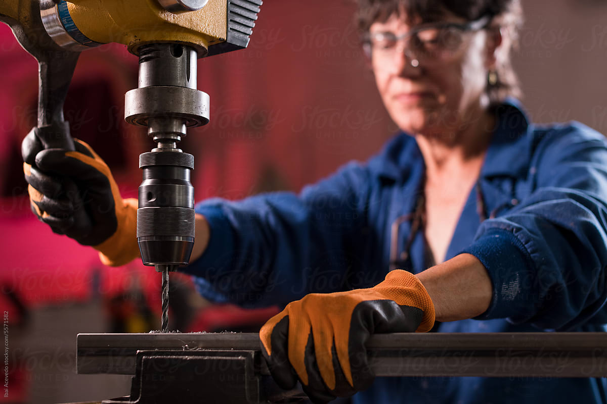 Mature woman working with industrial drill at workshop