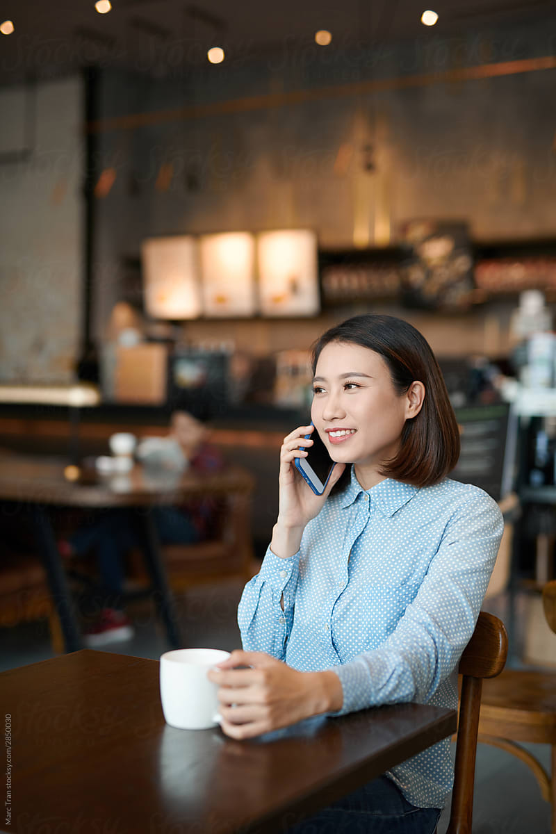 Asian woman talking on phone and drinking coffee