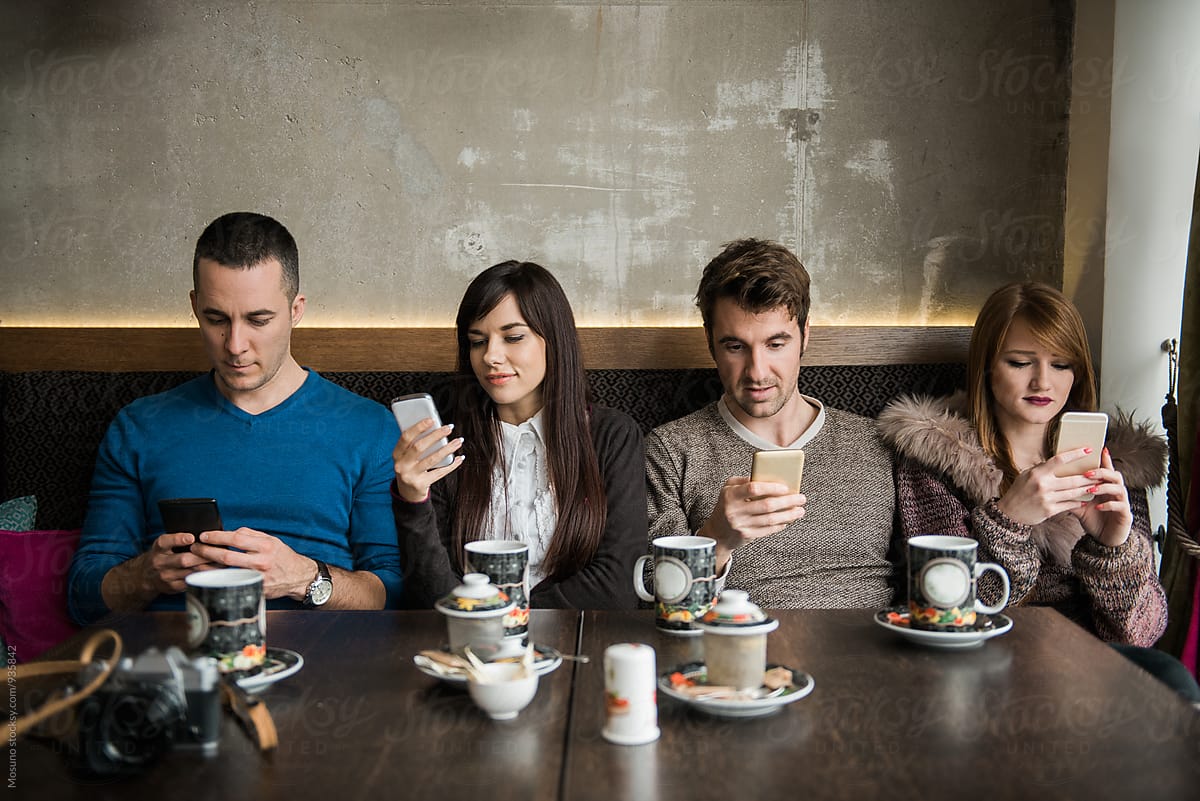 Four Friends Looking At Their Mobile Phone In A Cafe Del Colaborador De Stocksy Mosuno Stocksy 